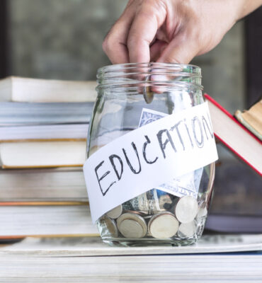 Coins and banknote in a glass jar placed on the textbook.