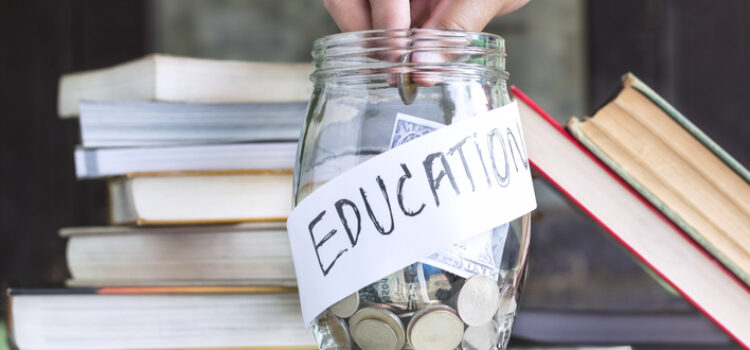 Coins and banknote in a glass jar placed on the textbook.